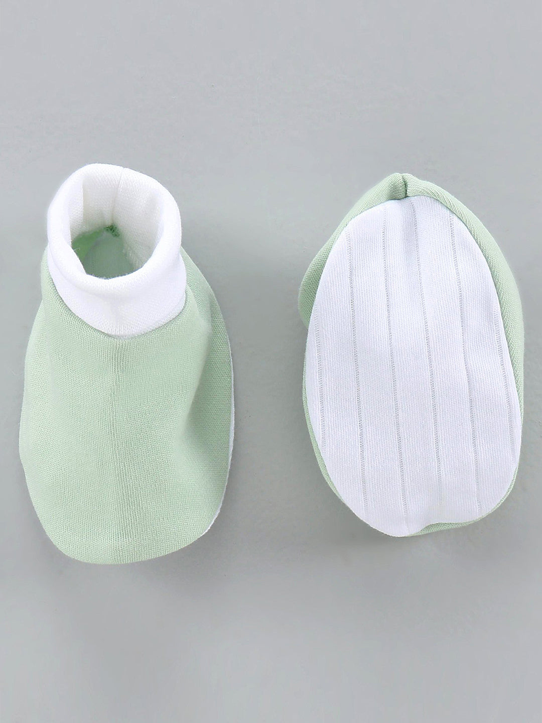 Pair of green baby booties with white soles on a gray background