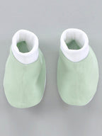 Pair of green baby booties with white tops on a gray background