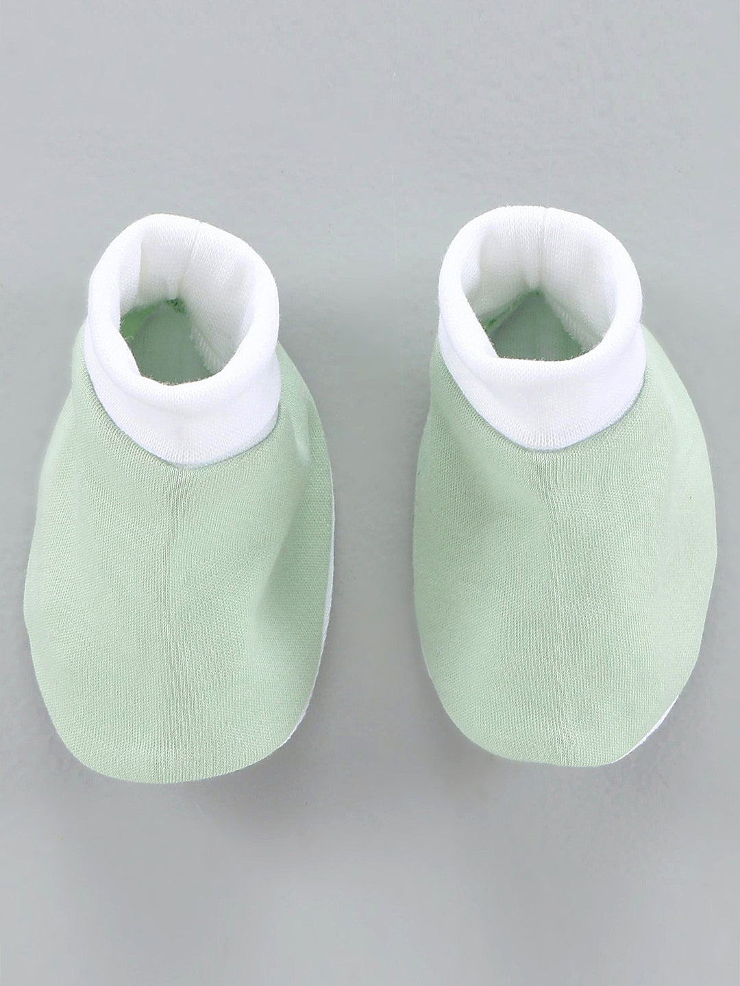 Pair of green baby booties with white tops on a gray background