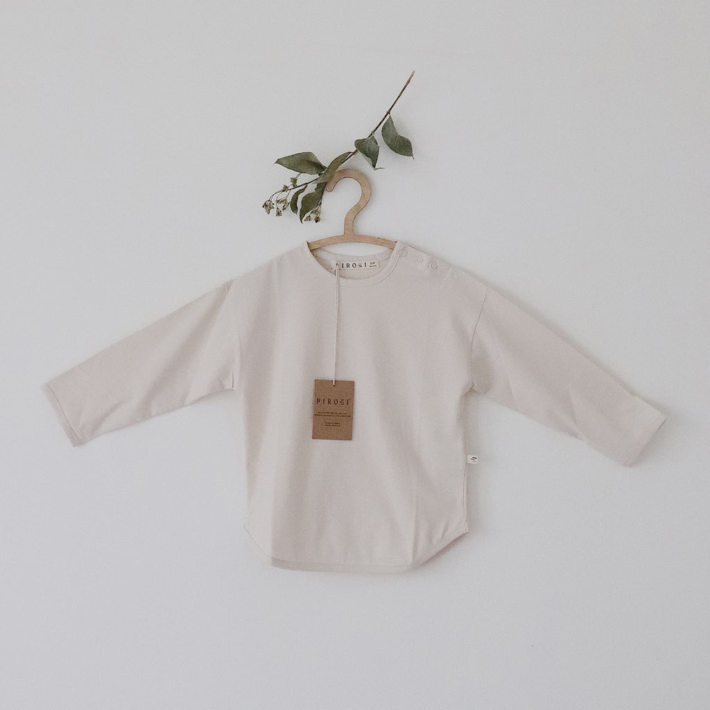 Beige baby shirt on a hanger with a plant branch against a light background