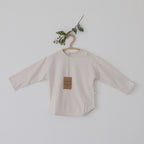 Beige baby shirt on a hanger with a plant branch against a light background