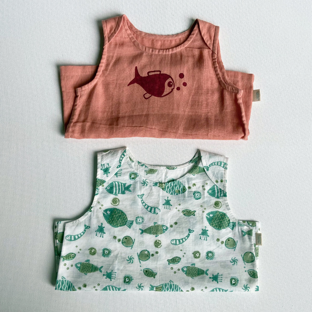 Two children's vests, one pink with a fish design and one green with fish pattern, on a light gray background.