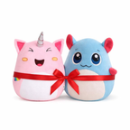 Two plush toys, one pink with a unicorn horn and the other blue with red accents, tied together with a red ribbon on a white background.